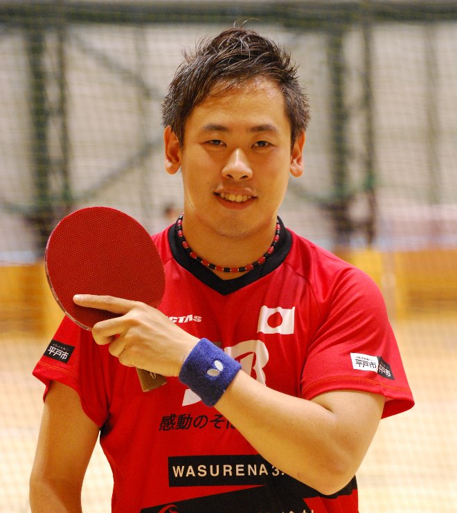 日本代表のユニフォームを着た男性が卓球ラケットを持って立っている写真
