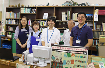 小川西町図書館の貸出しカウンターにエプロン姿の図書館職員が並んで写っている写真