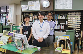 喜平図書館の貸出しカウンターにエプロン姿の図書館職員が並んで写っている写真