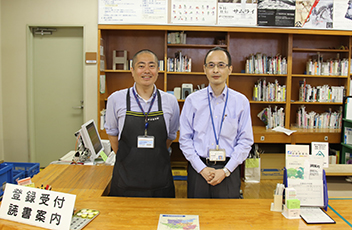 津田図書館の貸出しカウンターにエプロン姿の図書館職員が並んで写っている写真